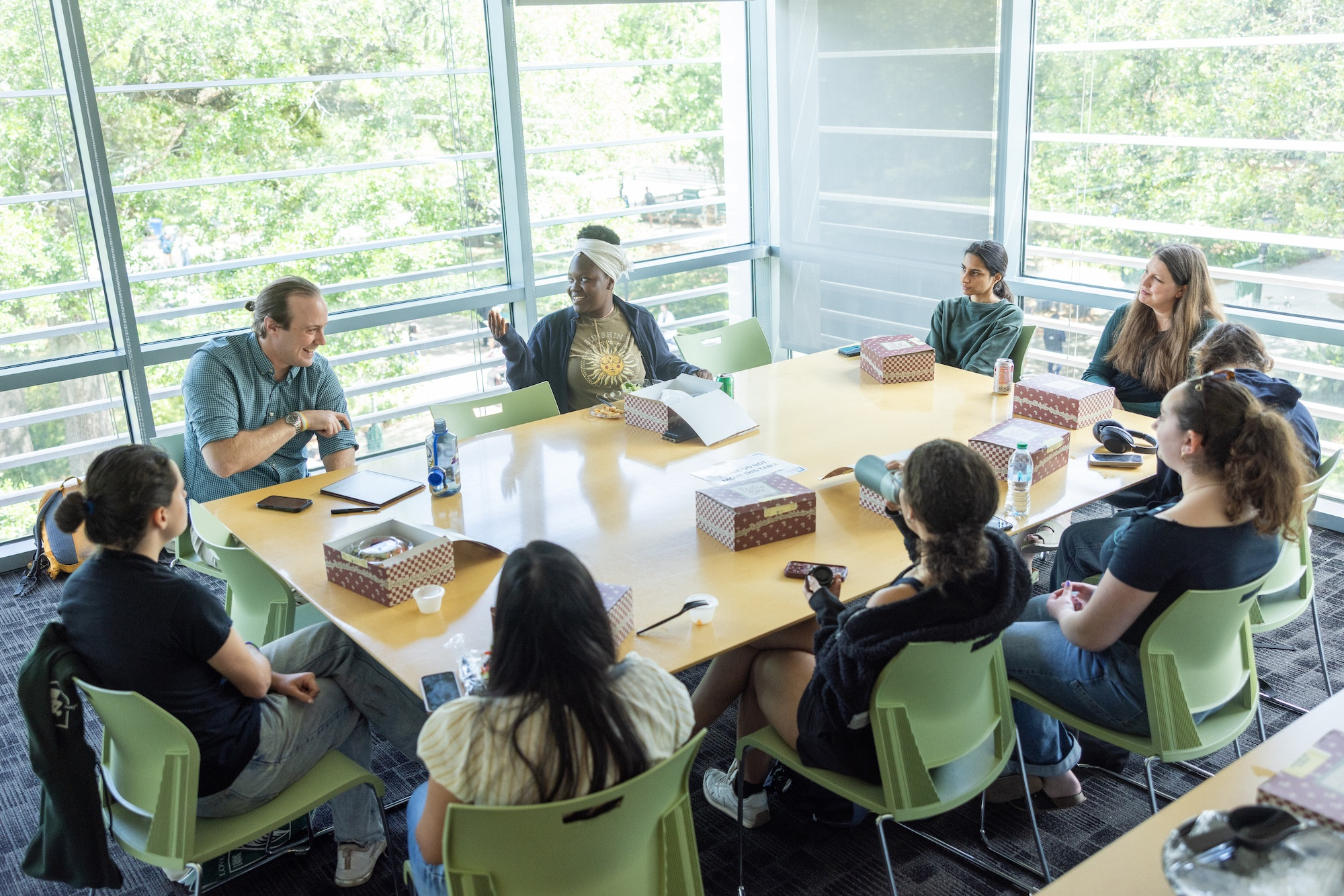 Group of people discussing around a table in a bright room with large windows. 
