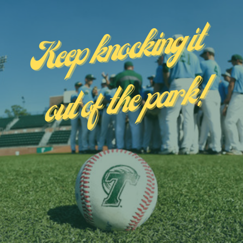 Baseball with a green 'T' logo on grass, blurry baseball team and stadium behind.